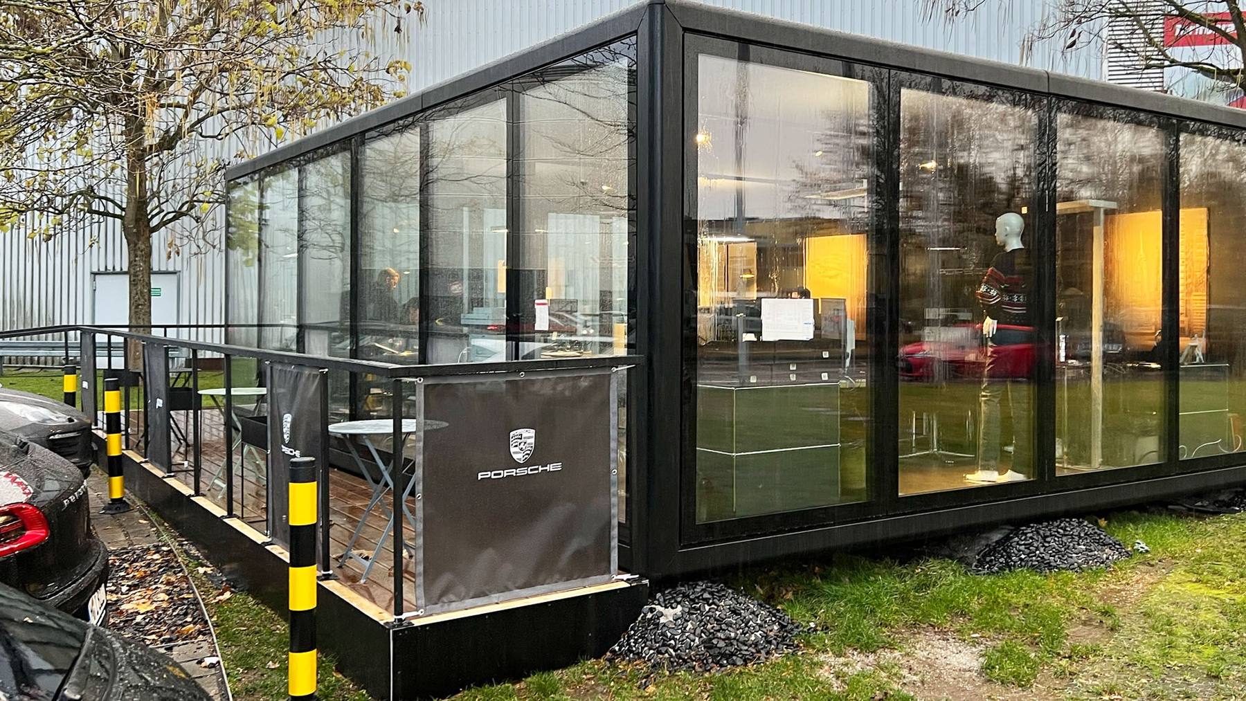 Aufnahme: KOYA Cube als modulare Ausstellungsfläche am Porsche Zentrum Aargau, schwarzer Modulbau mit raumhoher Verglasung im Herbst