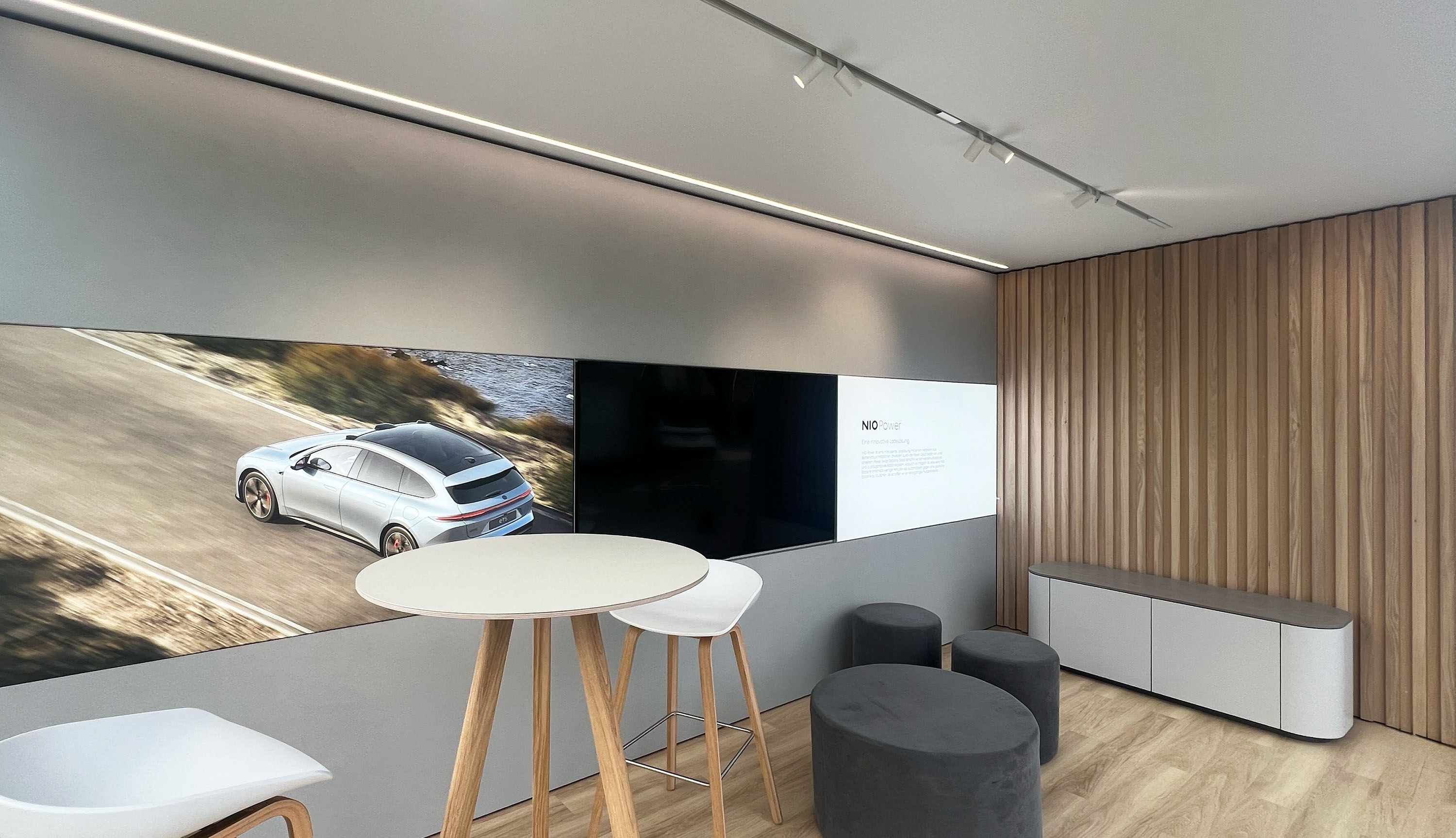 Innenraum eines KOYA Roadshow-Moduls mit Medienwand, Hochtisch, Holzlamellen an der Wand und Schienenstrahlern