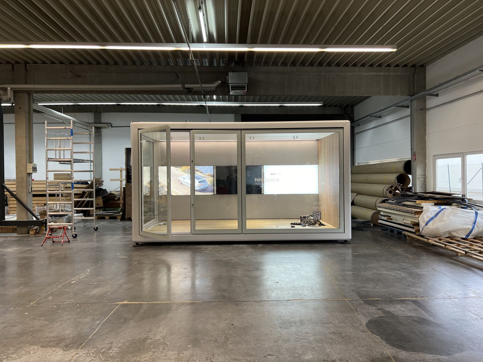 Modul mit hellem Rahmen, Glasfront und ausgebautem Innenraum mit Holzlamellen in der Werkhalle