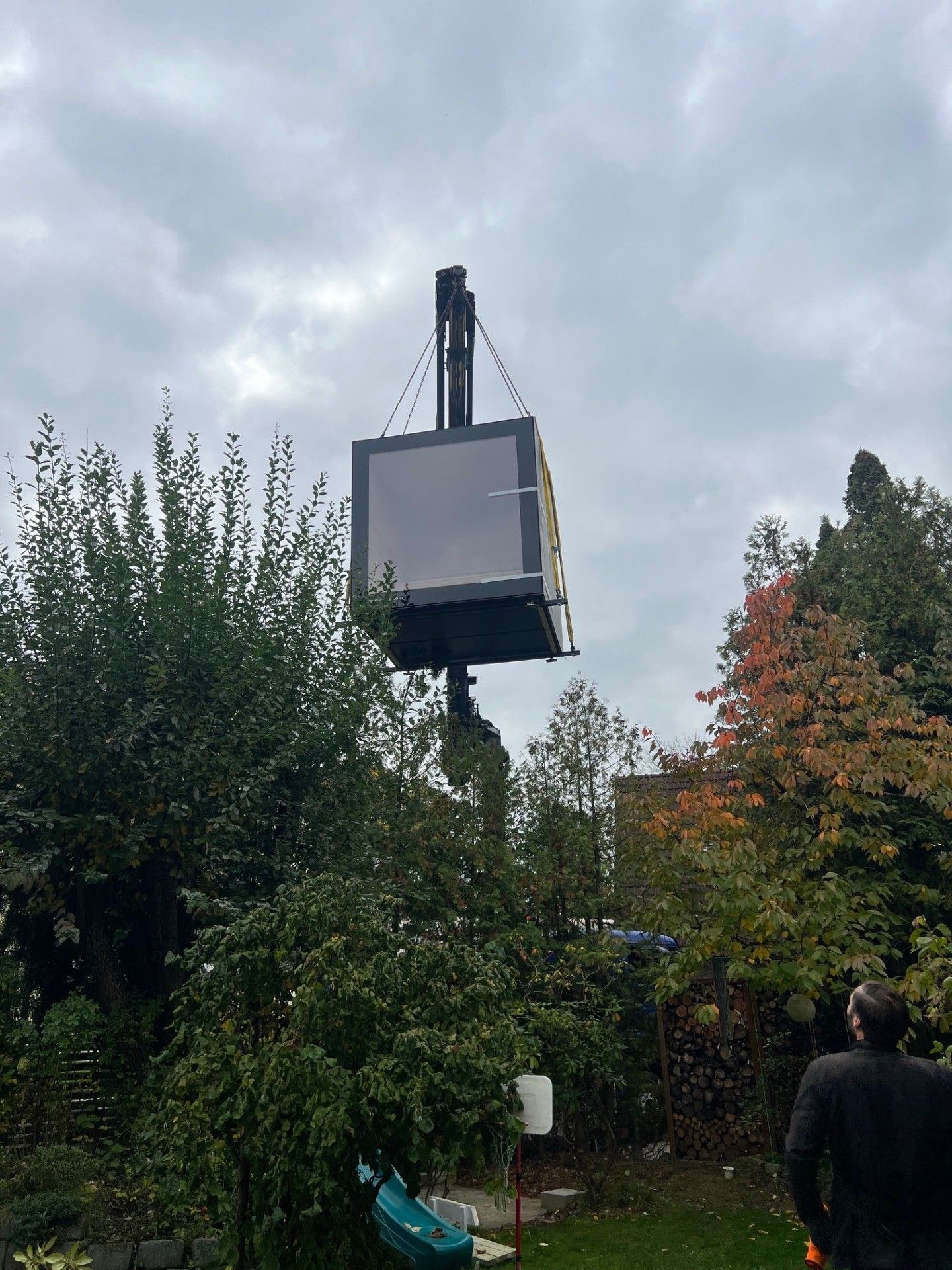 Aufnahme: Ein KOYA Sauna Cube schwebt am Kran über die Bäume in einen Garten