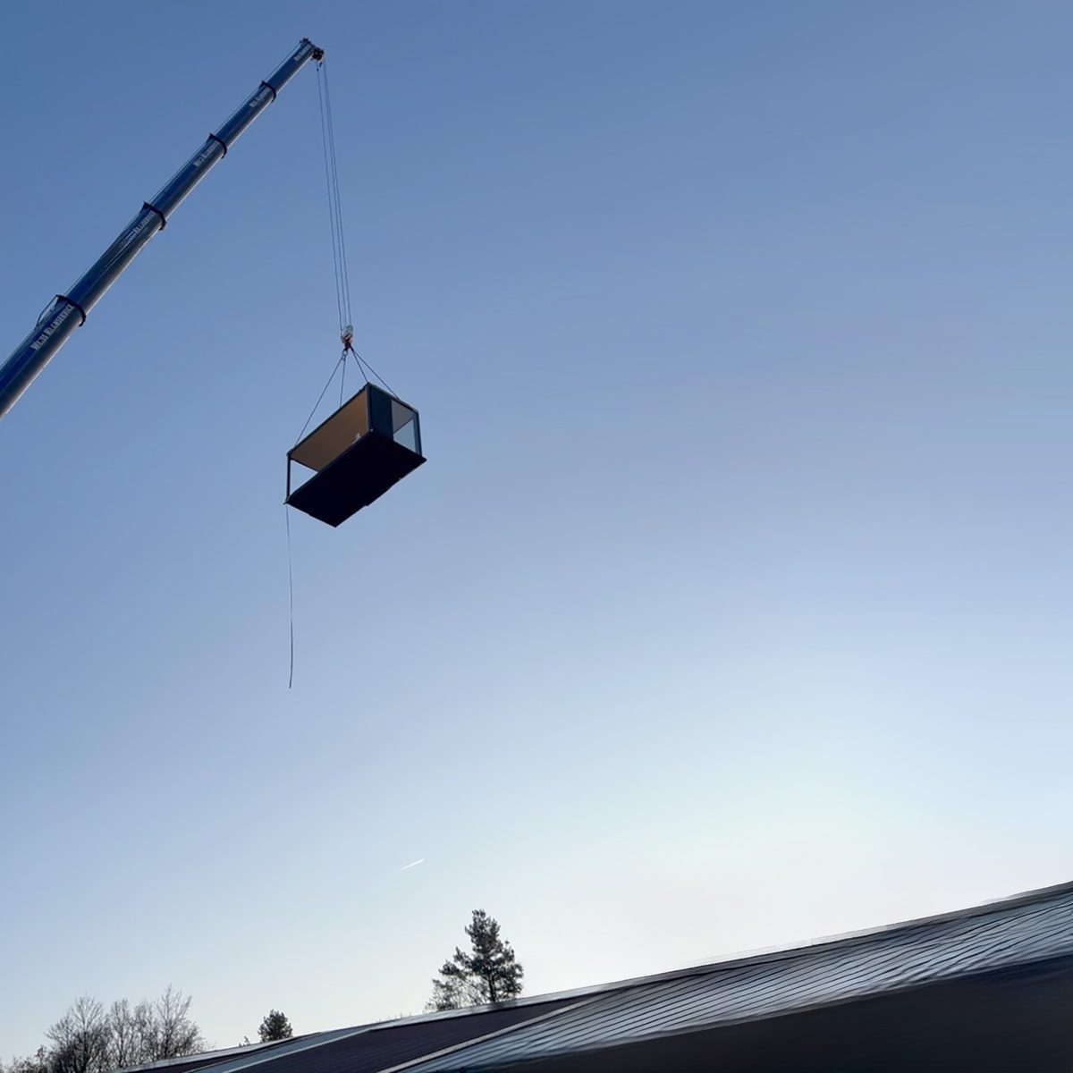 Ein KOYA Modul schwebt am Haken eines Autokrans vor blauem Himmel