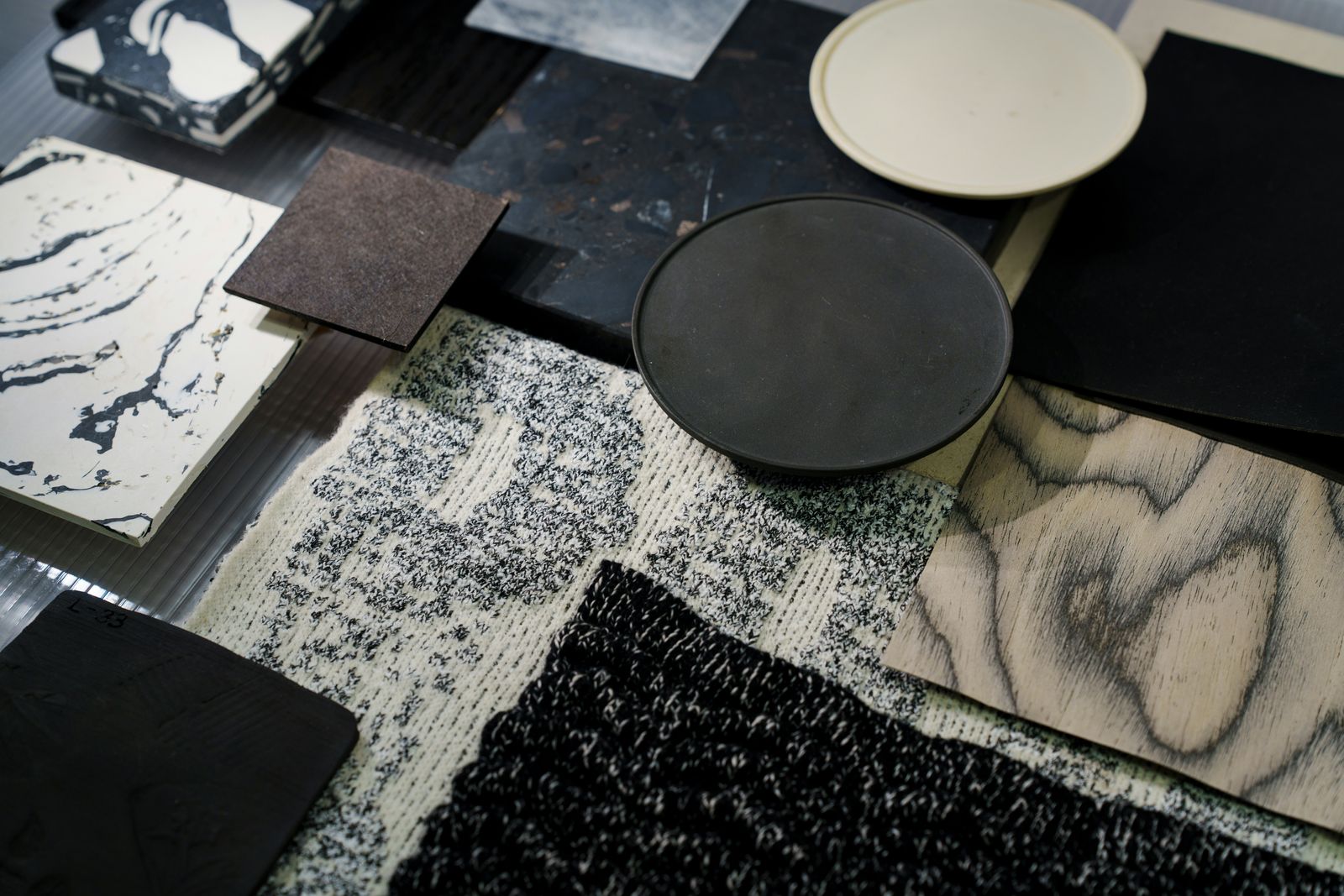 Materialmuster in Schwarz und Weiß: marmorierter Stein, Holzfurnier, runde Keramikschalen und Strickstoff